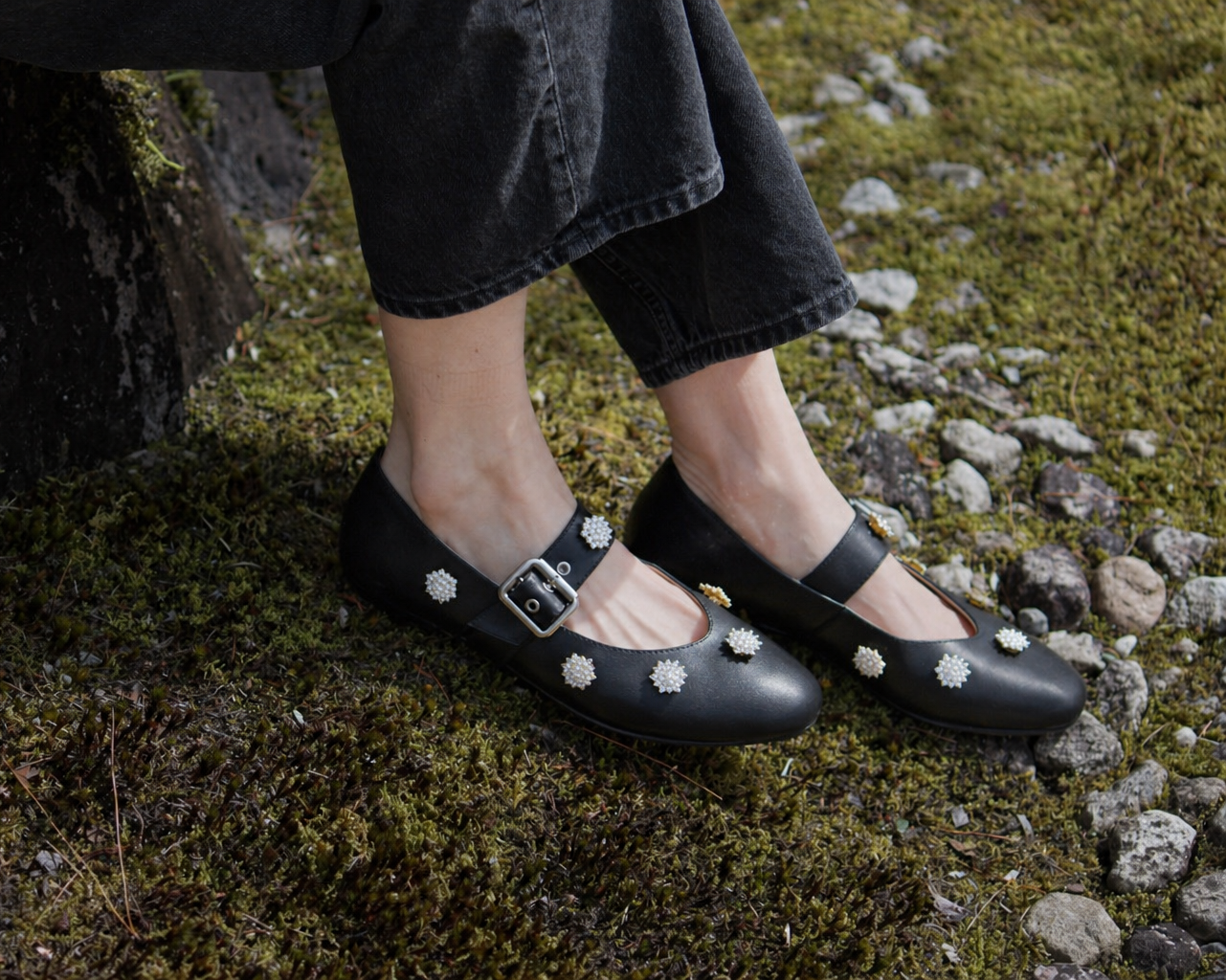 Black shoes with white floral patterns worn on a person's feet standing on a mossy ground.